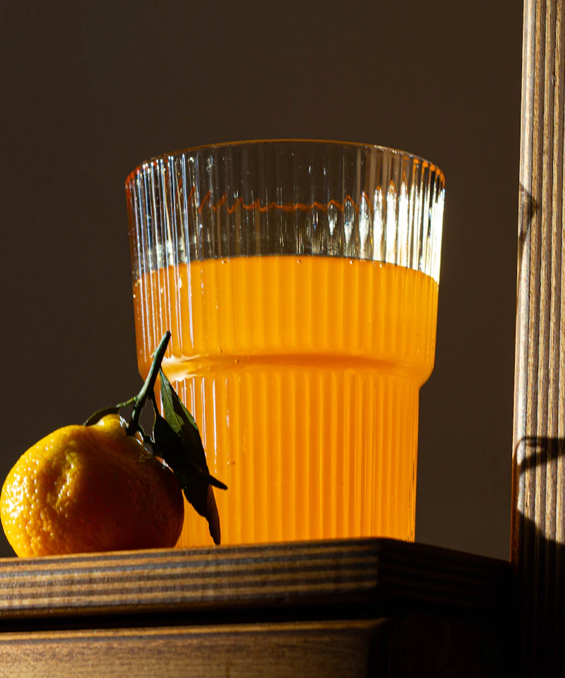 A ribbed glass of orange juice and a mandarin in warm directional sunlight